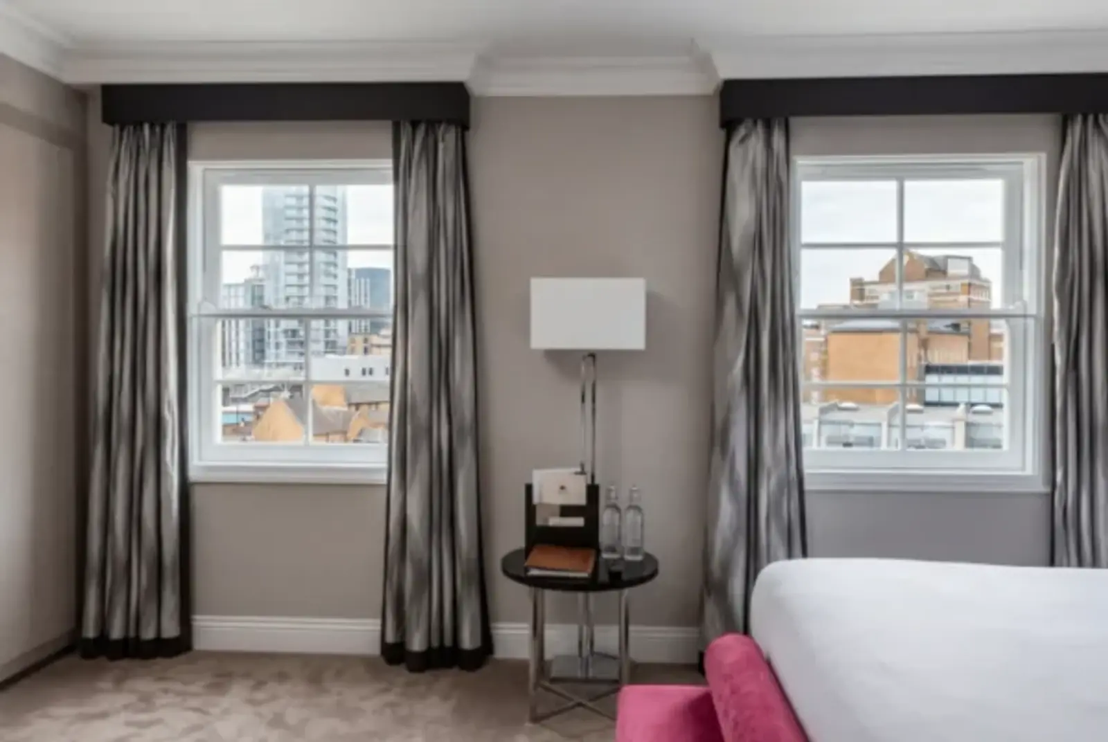 Finished bedroom with tall windows, curtains and city rooftops beyond