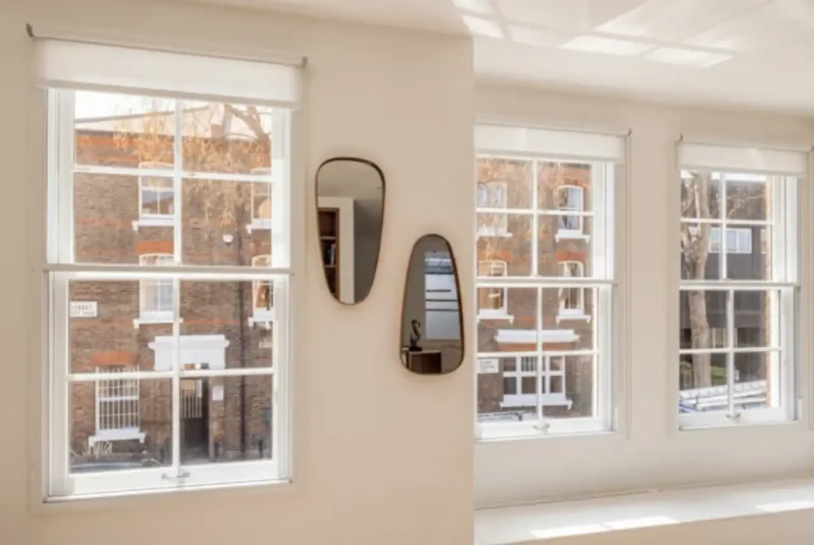 Bright period room with three sash windows, mirrors and a brick courtyard view